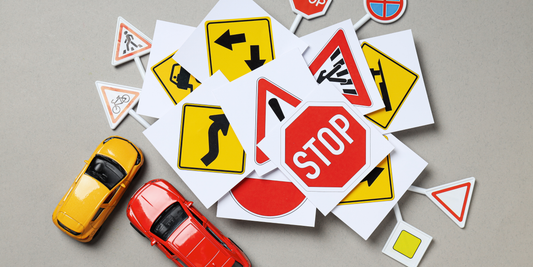A collection of Australian road signs scattered on a surface, accompanied by small toy cars, representing traffic rules and driving regulations